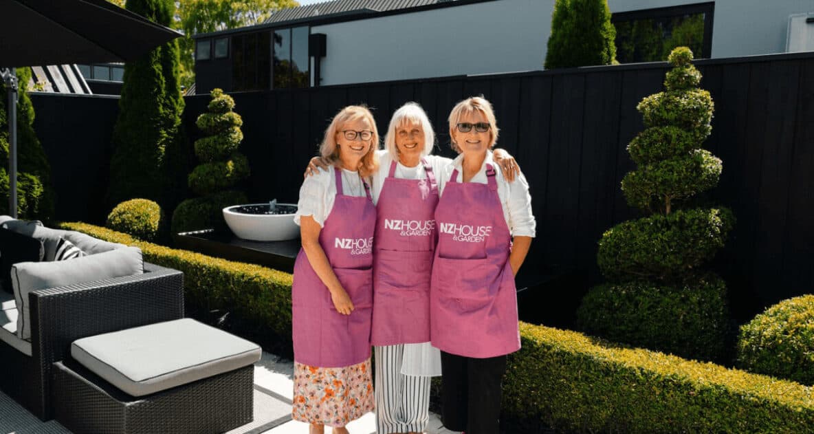 Three NZ House & Garden Tours volunteers in pink aprons in a home's garden